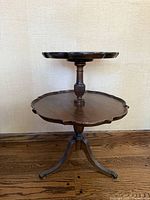 Full view of antique two-tier wooden tea side table with scalloped edges and claw feet