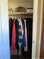 Photo of closet interior showing jackets hanging on wooden rod with boxes on top shelf.