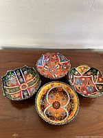 Four colorful handmade ceramic bowls with intricate floral and geometric designs on a wooden surface, photographed to show variety and detail of patterns.