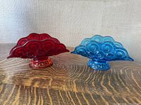 Both blue and red LE Smith glass banana boat fruit bowls side by side on wooden table.
