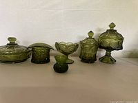 Six light green carnival glass items placed in a row on a white surface with a white backdrop, showcasing their shapes and textures.