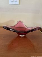 Side profile view of the pink Murano glass bowl showing its curved triangular shape and thick glass edges.