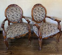 Pair of Victorian Revival mahogany cameo back parlor arm chairs with patterned fabric upholstery shown front view on hardwood floor.
