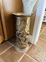 Side view of the brass umbrella stand showing embossed musicians and window