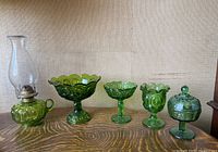 Front view of the lot showing all five green glass items on a wooden surface against a plain wall.