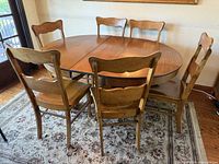Wide shot of the vintage oval dining table with 6 wooden chairs around it on a patterned rug.