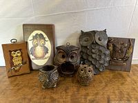 Front view of all 7 owl collectibles including plaques and ceramic figures arranged on wooden surface