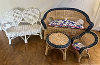 Four-piece wicker doll furniture set including a white heart-back loveseat, natural wicker loveseat and chair with cushions, and a small round table.