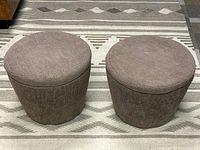 Two closed round brown fabric poufs on a patterned rug.