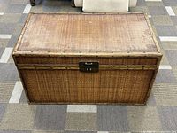 Front view of the closed bamboo woven storage chest showing medium brown color and tight weave pattern, with metal clasp closure