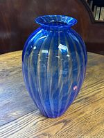 Blue tall Murano glass vase standing on wooden surface, showing its rounded shape and flared neck.