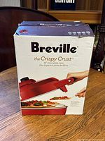 Photo of the Breville pizza oven box showing branding and product image on the front, highlighting the 12" stone pizza oven and crispy crust feature.