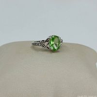Front angled view of silver ring with green glass rhinestone, showing Celtic knot detail and clear rhinestones on band.
