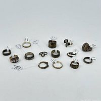 Front view of 14 assorted sterling silver rings arranged on white background, showing variety of designs.