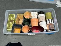 Top-down view of all 15 assorted small planters and containers inside a plastic storage bin.