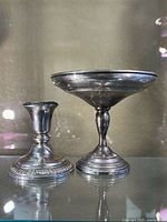 Pair of silver candlestick holders, one shorter with detailed circular base and the other taller with wide shallow top.