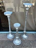 Wide shot showing all 3 silver textured metal pedestals of varying heights in front of window.