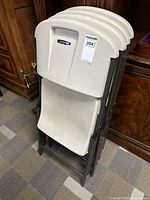 Stack of four Lifetime brand foldable plastic chairs folded and stacked