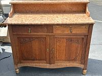 Wooden wash stand with marble top, two drawers, two cabinet doors, and carved detailing.