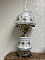 Full view of milk glass hurricane lamp showing floral patterns on white glass, metal base and clear chimney.