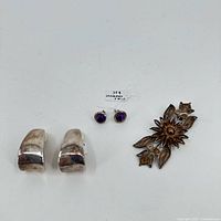 Photo showing all three items: silver half-hoop earrings, amethyst stud earrings, and floral sterling silver pin
