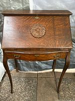 Front view of the Tiger Oak Secretary Desk showing the drop-front surface with carved medallion and curved legs.
