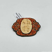 Front view of the vintage brooch showing a carved bone centerpiece with coral bead embellishment on a textured metal base.