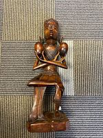 Full view of wooden carved seated figure statue placed on carpet showing overall form.