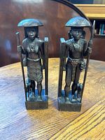 Front view of the wooden male and female figurine bookends on a wooden table, showing detailed carving and traditional attire.