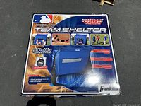 Photo of the boxed blue MLB pop-up team shelter with branding and images showing shelter in use and carry bag.
