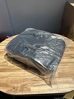 Single black football blocking dummy pad covered in transparent plastic wrap on a wood surface.