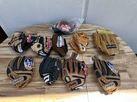 Overview of the 10 baseball gloves laid out on a wooden surface, showing mixed sizes and colors, mainly Franklin brand with one Spalding glove.
