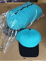 Photo of 16 marine green and black Richardson hats stacked in plastic packaging with one cap displayed outside to show full design.