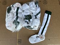 Two bags of white stirrup socks with black stripes laid out on a brown surface, showing bulk quantity and packaging.