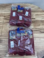 Photo showing multiple packs of burgundy Russell Athletic sports socks laid on a wooden surface, with visible packaging and labels.