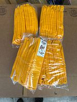 Four packs each containing six yellow tube socks folded and packaged in clear plastic bags on a cardboard surface.