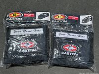 Photo of two Easton Championship Tote bags in original packaging placed side by side showing front pockets with 'Your Name Here' label and embroidered Easton logo.