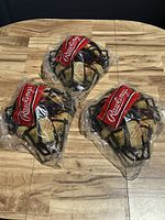 Group of 3 Rawlings catchers facemasks sealed in plastic, showing red Rawlings logo bands and black wire frames.
