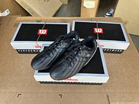 Three pairs of Wilson soccer cleats in black and silver on boxes, view of uppers