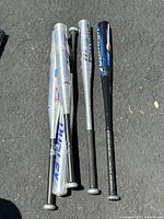 Five aluminum baseball bats laid on pavement, showing full length and grips.