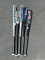 Group of 5 aluminum baseball bats laid on pavement showing barrels and grips
