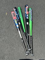 Top view showing group of five aluminum baseball bats arranged flat on pavement, displaying bat colors and grips.