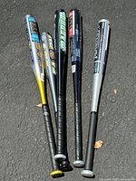 Top view of five aluminum baseball bats laid out on pavement showing various brands and colors