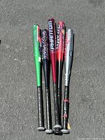 Five aluminum baseball bats laid on pavement, colors green, black, red, and silver, showing brand and model details.