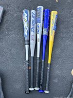 Five aluminum baseball bats laid out on ground showing brands and grips