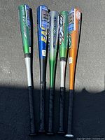 Photo showing five aluminum baseball bats with various colors and brands laid out side by side.