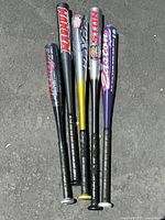 Photo of 5 aluminum baseball bats arranged side by side on pavement, showing various brand logos and colors.