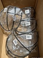 Five black metal faceguards wrapped in clear plastic packaging showing mounting screws and instructions.