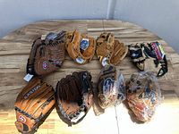 Group of 8 baseball gloves laid out on a wooden table showing variety of colors and sizes