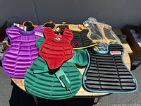Top view of the seven different catcher's pads arranged on a table in multiple colors: purple, red, green, black, yellow, and orange.